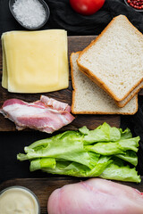 Ingredient for sandwich, bacon, cheese, tomato, chicken meat, lettuce, sauce, on black background, top view