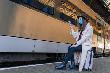 Fototapeta na wymiar Girl sitting on the platform of the train station and using smartphone