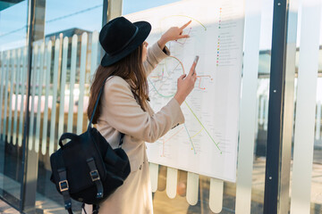 Woman tourist with phone in hand at bus stop looking on map of public transport routes