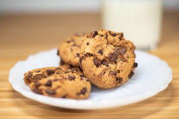 Chocolate chip cookies with a shallow dept of field, with glass of milk in the background, on a wooden table.