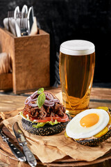 Set of hamburger with egg and beer. A standard set of drinks and food in the pub, beer and snacks. Dark background, fast food. Traditional american food.