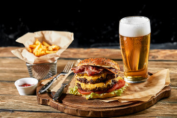 Set of hamburger beer and french fries. A standard set of drinks and food in the pub, beer and snacks. Dark background, fast food. Traditional american food.