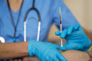 The nurse makes an injection with the vaccine to the patient at home. A young doctor in a blue suit...
