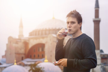 A young man drinks traditional Turkish tea on the background of the Hagia Sophia mosque. Great adventure and tourism in Turkey, Istanbul.