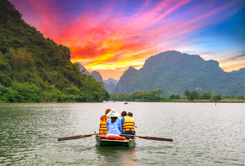 Ferry man rowing boats carrying tourists on river of the Tam Coc National Parkin sunset sky. This is a popular tourist destination in Ninh Binh, Vietnam.