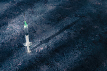 Syringe on blue wooden table with dark window shadows. Covid-19 vaccine concept year 2021. Coronavirus vaccine.