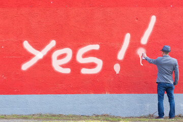 male is spraying graffiti Yes on a red wall and is positive