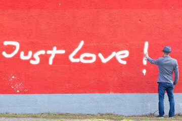 man is spraying graffiti just love on a red wall