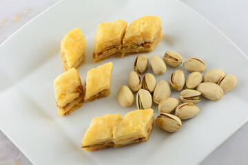 Pieces of baklava dessert with pistachio nuts on white snack plate