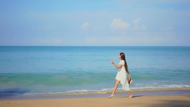 Beautiful girl walks on seashore dressed in white. Slow-motion