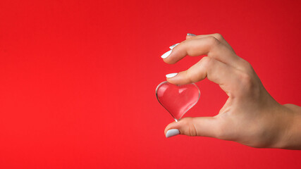The girl's hand gently holds a glass heart on a red background.