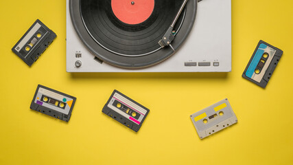 Fototapeta premium Scattered tape cassettes and a record player on a yellow background.