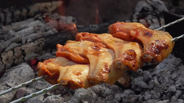 Close-up of the tasty chicken wings on the skewers are flipped above the open fire outdoors