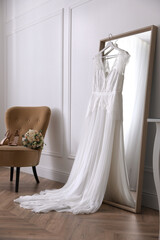 Elegant wedding dress hanging on large mirror in room