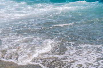 Fototapeta premium White foamy waves on sandy beach closeup. Seaside on sunny summer day. Summer vacation time concept.