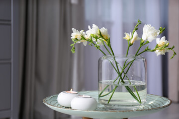 Vase with beautiful freesia flowers and burning candles on stand indoors, space for text. Interior...