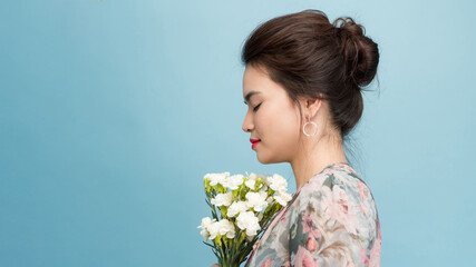 Sideways shot of pleased attractive young woman holds spring flowers, poses over pink background, has friendly smile on face, has romantic relationship with husband