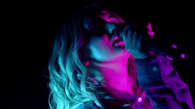Live vocal performance of emotional singer in darkness on black background. Vocalist girl in pink green neon light dancing, singing performing on concert musician stage. Party, music festival concert