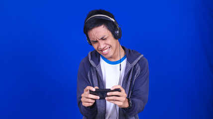 asian man playing mobile game with happy expression isolated blue background