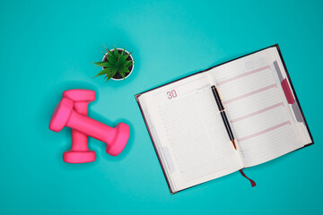 Workout plan in notebook. Flat lay of calendar plan with pink dumbbell, sport equipments, fitness items, top view with copy space. Healthy lifestyle and weight loss. Planning and management concept