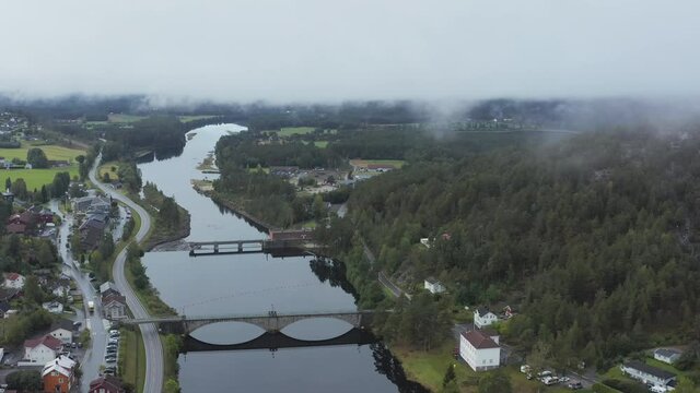 Aerial drone view over the Amfoss bridge on the Nidelva river,  in the Aamli town, dark, foggy day, in South Norway