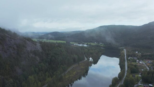 Aerial drone view of a reflecting river, town and hills, dark, foggy day, in Aamli, South Norway