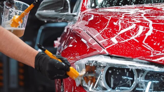 Auto cleaning service - man applying a cleaning solution on the red car
