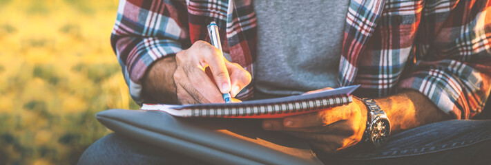 A man sitting write a book on the lawn in the park