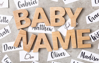Paper sheets with different baby names and wooden letters on grey background, flat lay
