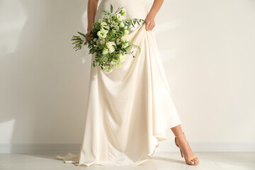 Fototapeta na wymiar Young bride wearing wedding dress with beautiful bouquet near light wall, closeup