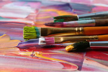 Fototapeta premium Set of different brushes on abstract colorful paint, closeup
