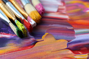 Fototapeta premium Set of different brushes on abstract colorful paint, closeup