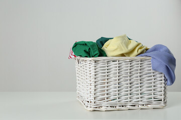 Wicker laundry basket with different clothes on light background. Space for text