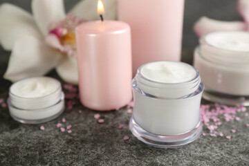 Beautiful spa composition with cosmetic products, candle and flower on grey table, closeup