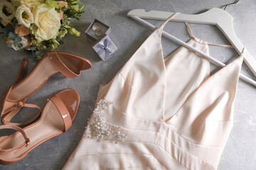 Flat lay composition with beige wedding dress and engagement rings on grey marble table