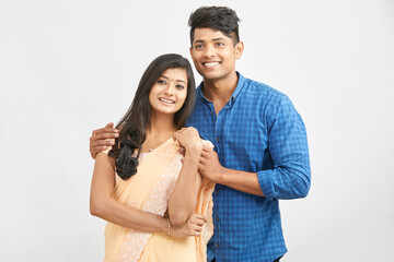 Cheerful Indian young couple in traditional outfit against white.