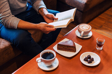 Fototapeta na wymiar Persona sentada leyendo mientras toma café con un postre