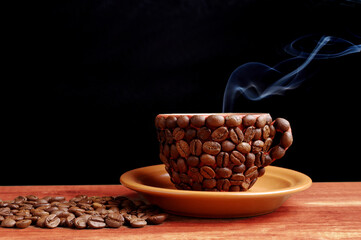 Hot coffee cup made from coffee beans with steam smoke on dark background.