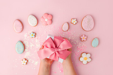 Colorful easter cookies with icing and gifr box in kid hands on pink background, colorful seasonal holiday concept, stylish greeting card, invitation, flyer. copy space, banner