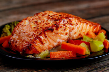 Baked juicy salmon fillet with steamed vegetables on black plate.