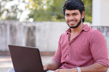 Smiling young man with laptop and looking at the camera on terrace.