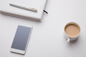 Headphone, coffee cup, smartphone with note and pen on table.