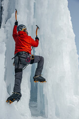 Alpinist man with ice tools axe climbing a large wall of ice. Outdoor Sports Portrait.