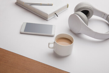 Headphone, coffee cup, smartphone with note and pen on table.