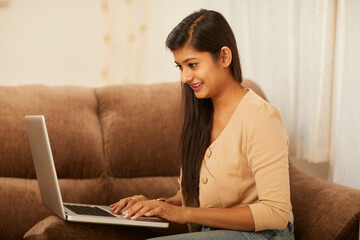 Young woman working on laptop at home on sofa
