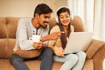 Happy young couple using laptop at home on sofa.