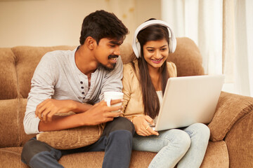 Obraz premium Happy young couple using laptop at home on sofa.