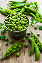 Fresh green peas in a small metal bucket on old wooden background.