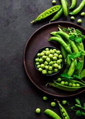 Green peas in  bowl with fresh pods on the black concrete background, top view or flat lay