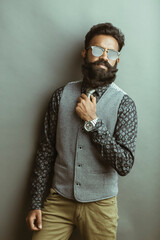 Bearded young businessman posing with sunglasses on gray.